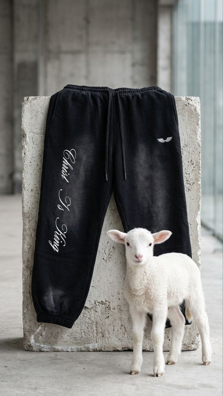 Apostles Apparel premium heavyweight Christian streetwear sweatpants featuring Christ Is King script embroidery next to a small white lamb in a minimalist architectural setting.