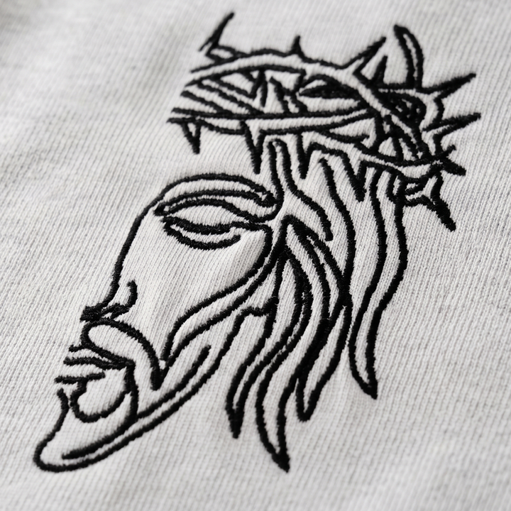 Macro close-up shot of the high-stitch count Christ Half Face line-art embroidery on the Apostles Apparel Foundations Unisex Oversized Ultra Heavy Crew Neck in Heather Grey. Displays the precise black thread stitchwork against the 425GSM premium heavyweight 100% cotton fabric.