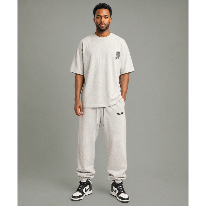 Model streetwear outfit shot featuring Apostles Apparel Foundations Unisex Oversized Ultra Heavy Crew Neck and matching joggers in Heather Grey. Displays the architectural drop-shoulder drape, 425GSM heavyweight plush cotton fabric premium fit, and Christ Half Face line-art embroidery detailing.