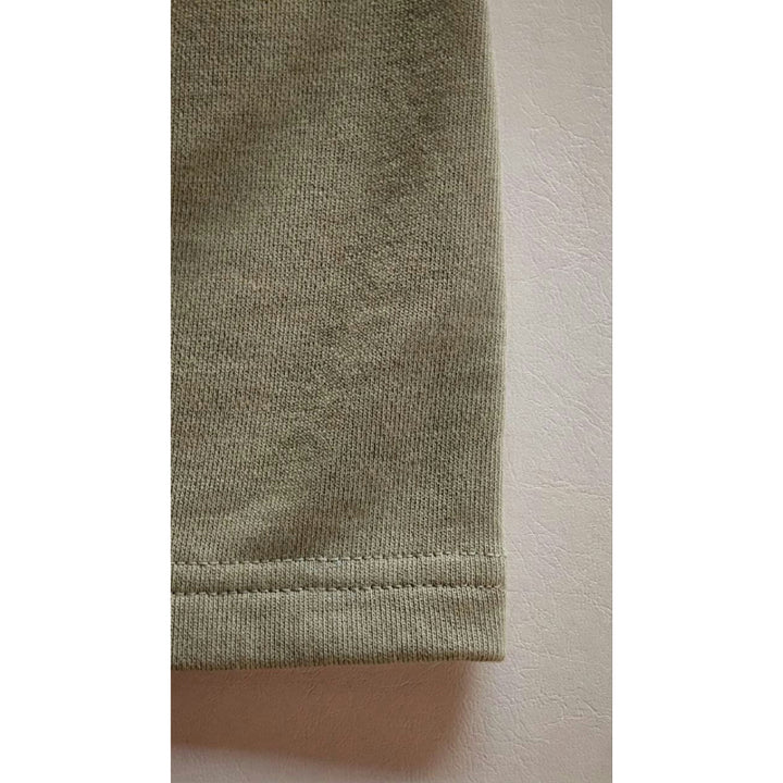 Macro detailing shot of the Christian Apparel Foundations Series Heavyweight Unisex Sweat Short in artichoke green. Close-up tightly captures the clean execution of the durable double-needle coverstitch cuff hem, highlighting the massive structural density and tight grain texture of the premium 425GSM combed cotton French terry fabric.
