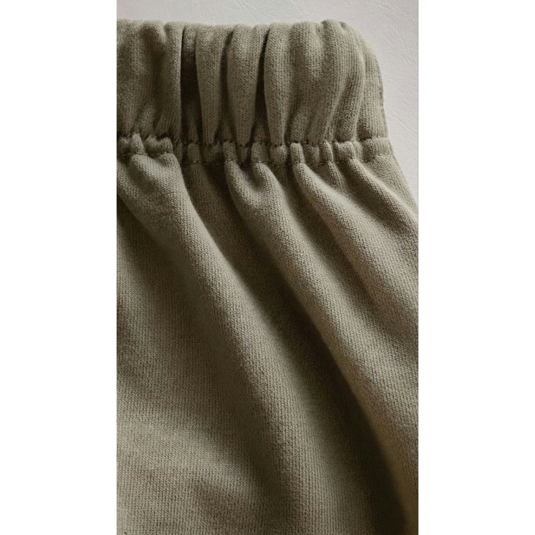 Macro detailing shot of the Christian Streetwear Foundations Series Heavyweight Unisex Sweat Short in artichoke green. Close-up tightly captures the overbuilt single-casing topstitched waistband gather, highlighting the thick structural texture and heavy drape of the premium 425GSM combed cotton French terry fabric weave.