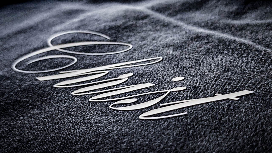 Macro close-up detailing shot of the Foundations Series Christ Is King Sun-Faded Heavyweight Pant in black. Dramatic angle showcases the high-density matte white graphic calligraphy lettering resting flat against the premium 400GSM combed cotton brushed fleece, highlighting the razor-sharp zero-gloss print texture.
