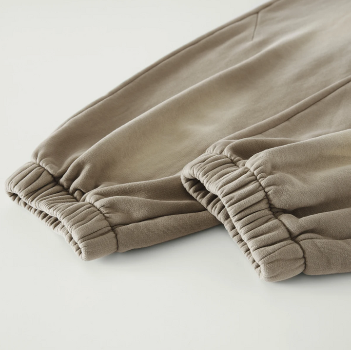 Macro detailing shot of the Foundations Series Christ Is King Sun-Faded Heavyweight Pant in smoky camel. Close-up highlights the elasticized stacking ankle cuffs, structural panel stitching, and the dense drape of the premium 400GSM combed cotton brushed fleece fabric.