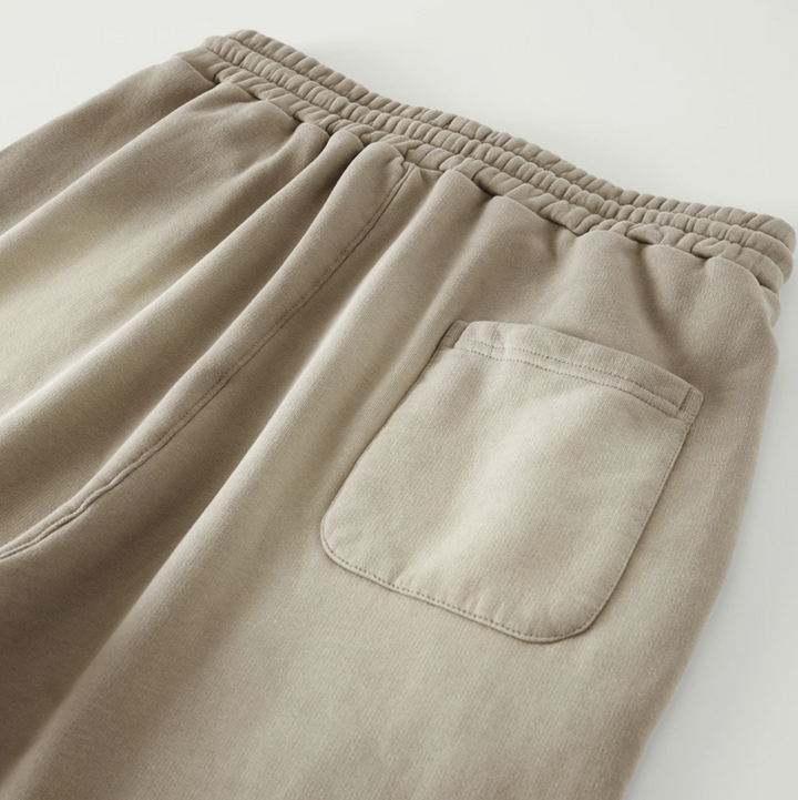 Rear macro detailing shot of the Foundations Series Christ Is King Sun-Faded Heavyweight Pant in camel. Close-up highlights the single rear patch utility pocket with reinforced topstitching, the architectural 3-tiered elastic waistband, and the heavy drape of the premium 400GSM combed cotton brushed fleece fabric.