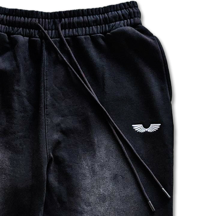 Macro detailing shot of the Foundations Series Christ Is King Sun-Faded Heavyweight Pant in smokey black. Close-up showcases the structural 3-tiered topstitched waistband, heavy-gauge drawstrings equipped with premium black soft-touch matte aglets, and a high-contrast white embroidered brand wings logo against the sun-faded 400GSM combed cotton brushed fleece chassis.