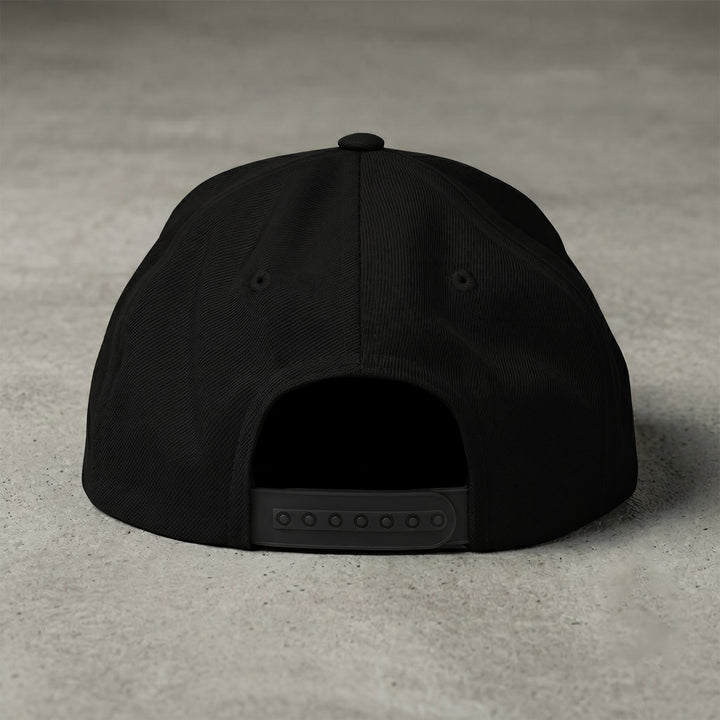 Rear studio view of the Foundations Series Christ Is King Triple Black Signature Snapback by Apostles Apparel on a concrete surface. Highlights the adjustable plastic snap closure, structured rear panels, precision-embroidered ventilation eyelets, and premium heavyweight wool-blend texture.