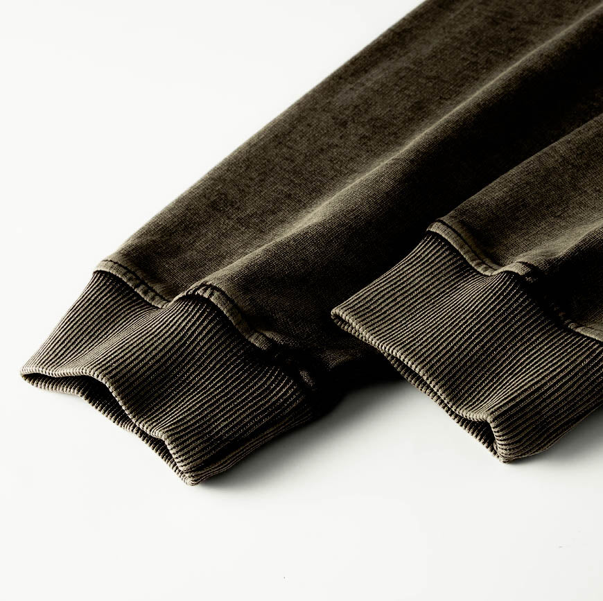Macro detailing shot of the Foundations Series 70X7 Raw Hem Long Sleeve in a sun-faded black tone. Close-up highlights the premium construction of the double-stitched ribbed collar and reinforced cuffs, showcasing the multi-dimensional washed texture of the heavy 260GSM enzyme-washed combed cotton fabric for a premium Christian clothing piece.