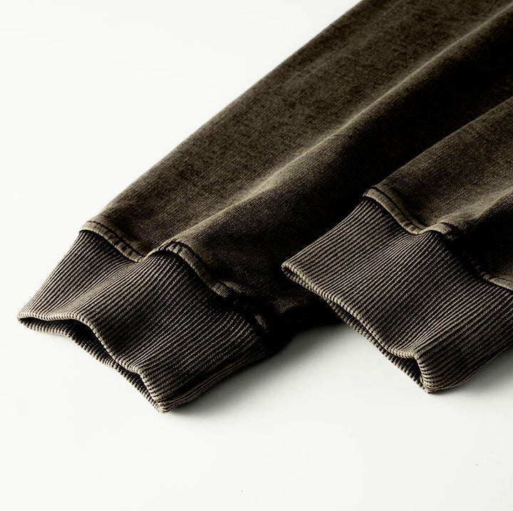 Macro detailing shot of the Foundations Series 70X7 Raw Hem Long Sleeve in a sun-faded black tone. Close-up highlights the premium construction of the double-stitched ribbed collar and reinforced cuffs, showcasing the multi-dimensional washed texture of the heavy 260GSM enzyme-washed combed cotton fabric for a premium Christian clothing piece.