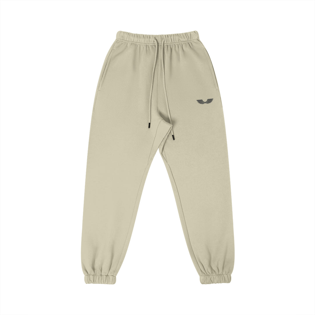 Front studio flat lay view of the Foundations Series Heavyweight Unisex Brushed Fleece Jogger in a soft camel tone, designed as premium Christian streetwear. Features high-density black Wings Emblem premium embroidery on the left thigh, an overbuilt single-casing comfort waistband with heavy-gauge cotton drawstrings and black metal aglets, and gathered ankle cuffs on a structural 380GSM combed cotton relaxed tapered canvas for mission-driven Christian clothing and apparel.
