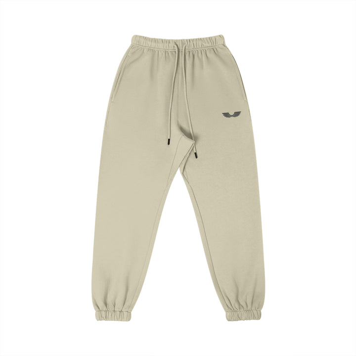 Front studio flat lay view of the Foundations Series Heavyweight Unisex Brushed Fleece Jogger in a soft camel tone, designed as premium Christian streetwear. Features high-density black Wings Emblem premium embroidery on the left thigh, an overbuilt single-casing comfort waistband with heavy-gauge cotton drawstrings and black metal aglets, and gathered ankle cuffs on a structural 380GSM combed cotton relaxed tapered canvas for mission-driven Christian clothing and apparel.