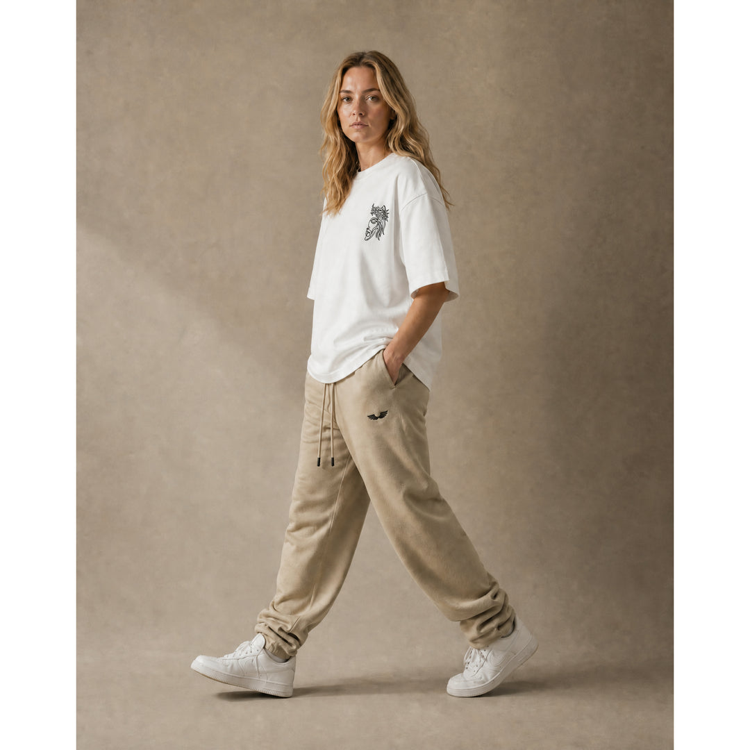 Full-body lifestyle model view showcasing the Foundations Series Heavyweight Unisex Brushed Fleece Jogger in a soft camel tone paired with the Unisex Embroidered Boxy Tee in white. Captures the relaxed oversized tapered jogger silhouette with technical stacking at the ankle cuffs alongside the modern dropped-shoulder draped tee, delivering a complete premium Christian streetwear outfit for mission-driven Christian clothing and pro-life apparel.