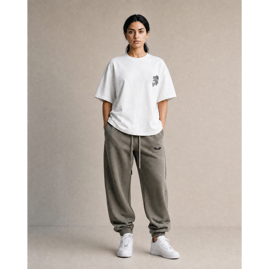 Full-body studio lifestyle model view showcasing the Foundations Series Unisex Embroidered Boxy Tee in white paired with the Heavyweight Unisex Brushed Fleece Jogger in charcoal grey. Captures the architectural boxy drape and dropped shoulders of the 280GSM tee featuring the high-stitch count Christ Half Face line-art embroidery on the chest, styled with the relaxed tapered streetwear jogger silhouette for a complete mission-driven Christian clothing statement.
