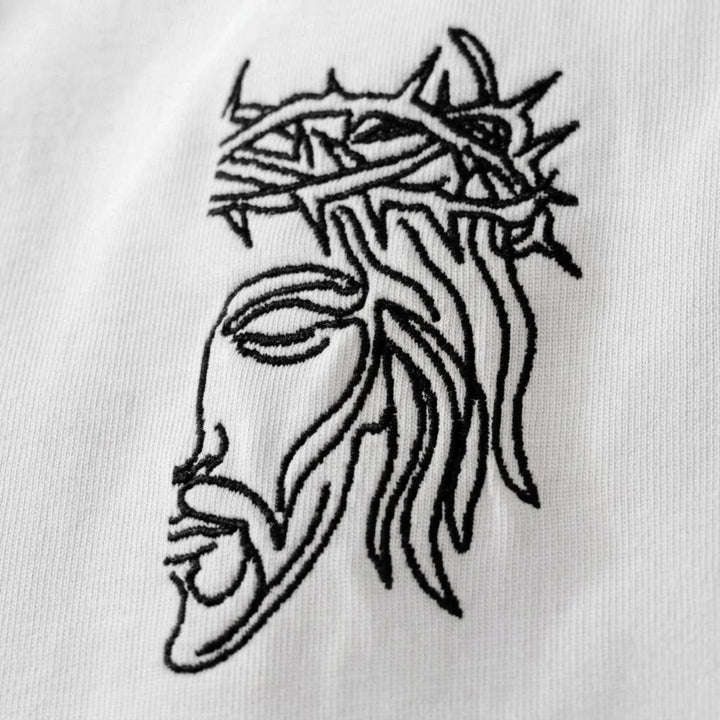 Macro detailing shot of the Foundations Series Unisex Embroidered Boxy Tee in white. Close-up tightly captures the high-stitch count Christ Half Face line-art embroidery on the front chest, showcasing the precision black needlework contrasting clearly against the luxury soft-touch brushed texture of the heavy 280GSM combed cotton fabric for a premium Christian clothing statement.
