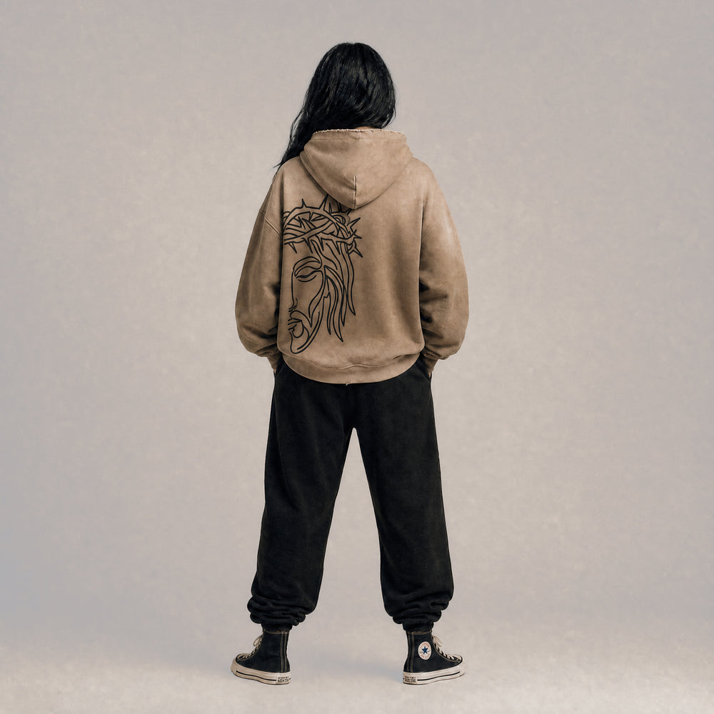 Full-body lifestyle model view from the back wearing the Apostles Apparel Foundations Crown of Thorns Heavyweight Hoodie in faded and distressed camel. Displays the signature boxy oversized silhouette with dropped shoulders, highlighting the raw streetwear drape and the jumbo line-art back screen print.