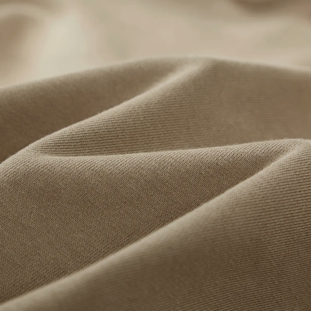Macro textile shot of the Foundations Series Crown of Thorns Heavyweight Hoodie in faded and distressed camel. Close-up tightly captures the tight weave of the 440GSM ultra-dense 100% combed cotton, highlighting the heavy premium surface structure and the custom pigment-dyed, stone-washed finish.