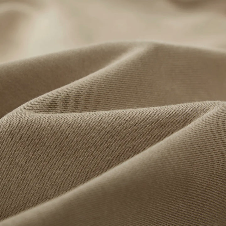 Macro textile shot of the Foundations Series Crown of Thorns Heavyweight Hoodie in faded and distressed camel. Close-up tightly captures the tight weave of the 440GSM ultra-dense 100% combed cotton, highlighting the heavy premium surface structure and the custom pigment-dyed, stone-washed finish.