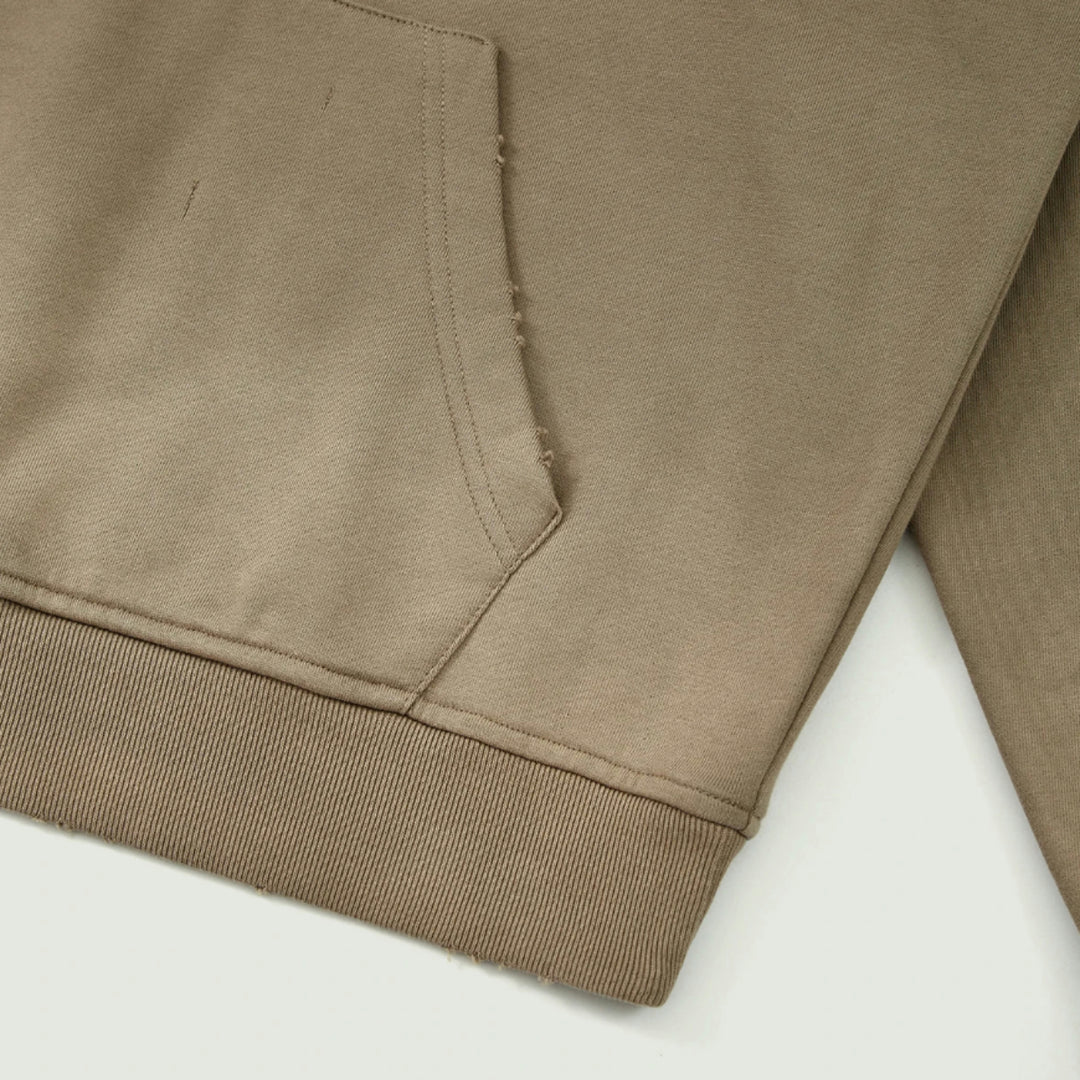 Macro detailing shot of the Foundations Series Crown of Thorns Heavyweight Hoodie in faded and distressed camel. Close-up highlights the side-seamed construction, kangaroo pouch pocket stitching, 1x1 heavy rib knit hem, and precise hand-distressed grinding along the seams and edges.