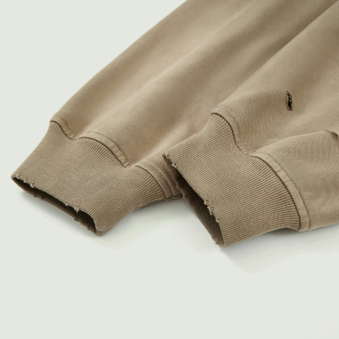 Macro detailing shot of the Foundations Series Crown of Thorns Heavyweight Hoodie in faded and distressed camel. Close-up highlights the custom hand-distressed grinding on the heavy 1x1 rib knit cuffs, dense 440GSM combed cotton fabric weave, and custom stone-washed vintage patina.