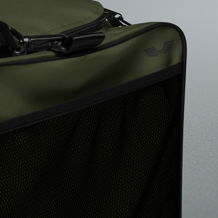 Macro detailing shot of the Foundations Series Let God Carry It Utility Duffle Bag in olive green. Close-up showcases the exterior quick-access side mesh pocket, the subtle tonal wings brand logo print, heavy-duty shoulder strap metal clip attachments, and reinforced black trim architecture.