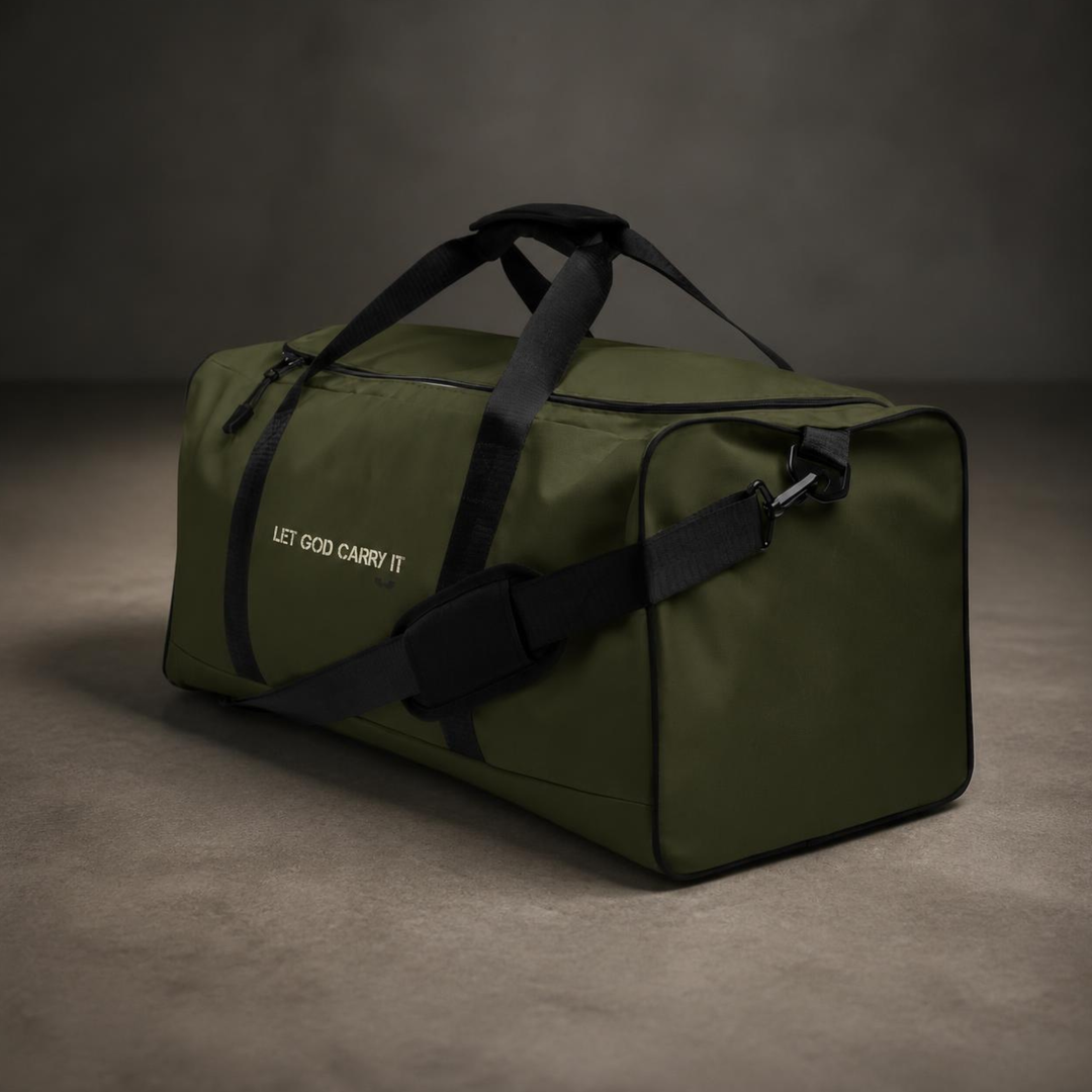 Three-quarter studio view of the Foundations Series Let God Carry It Utility Duffle Bag in olive green on a concrete floor. Highlights the adjustable and removable padded shoulder strap with heavy-duty clips, dual padded handles, rigid reinforced T-piping design, and architectural typography.